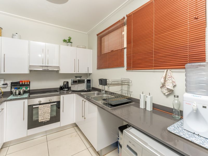A functional kitchen featuring white gloss cabinetry, stone countertops, built-in oven, electric hob, and a stainless steel double sink with tiled flooring.