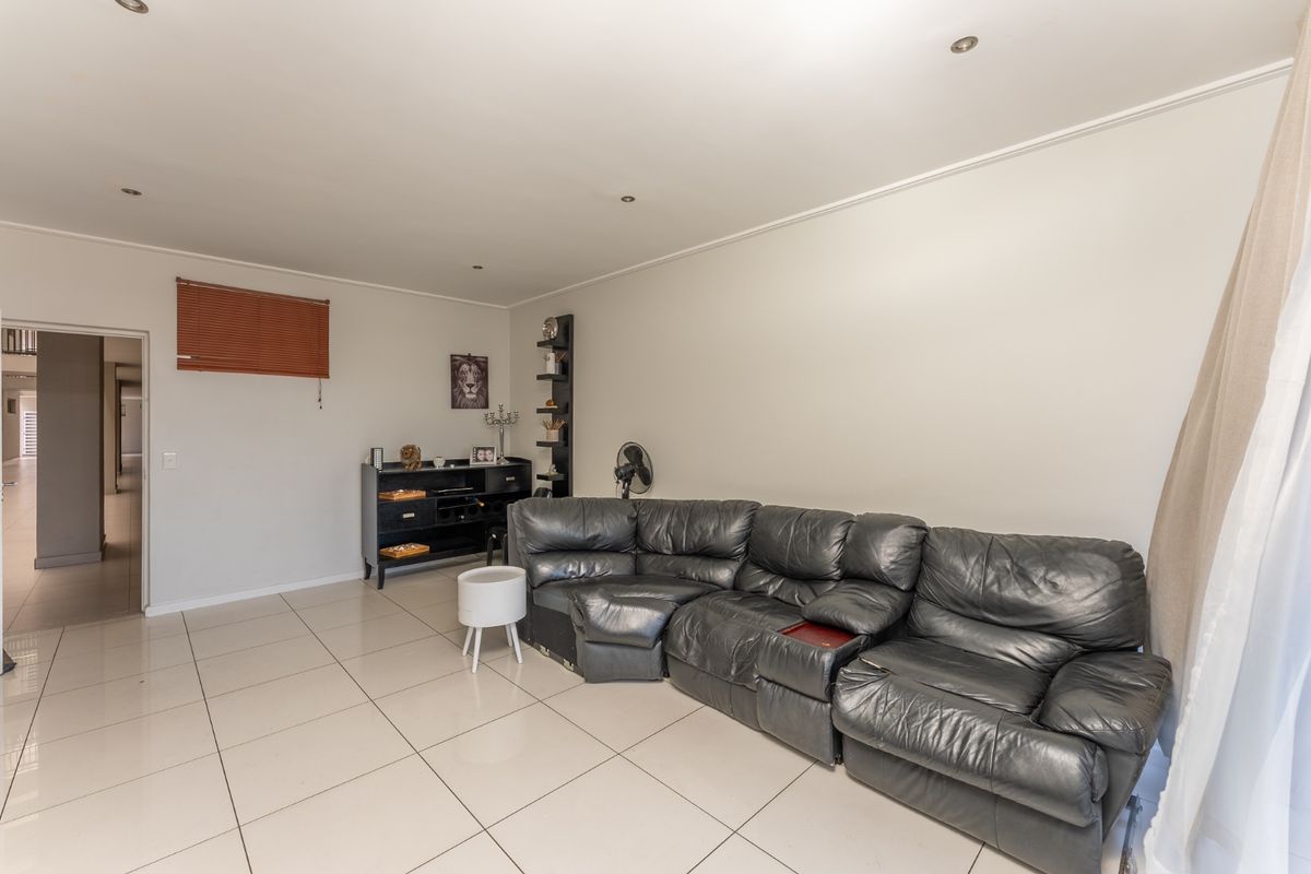A spacious living room featuring neutral tiled flooring, recessed downlighting, and a window with a fitted venetian blind.