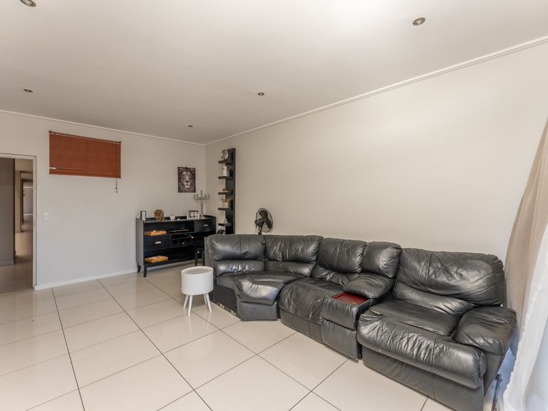 A spacious living room featuring neutral tiled flooring, recessed downlighting, and a window with a fitted venetian blind.