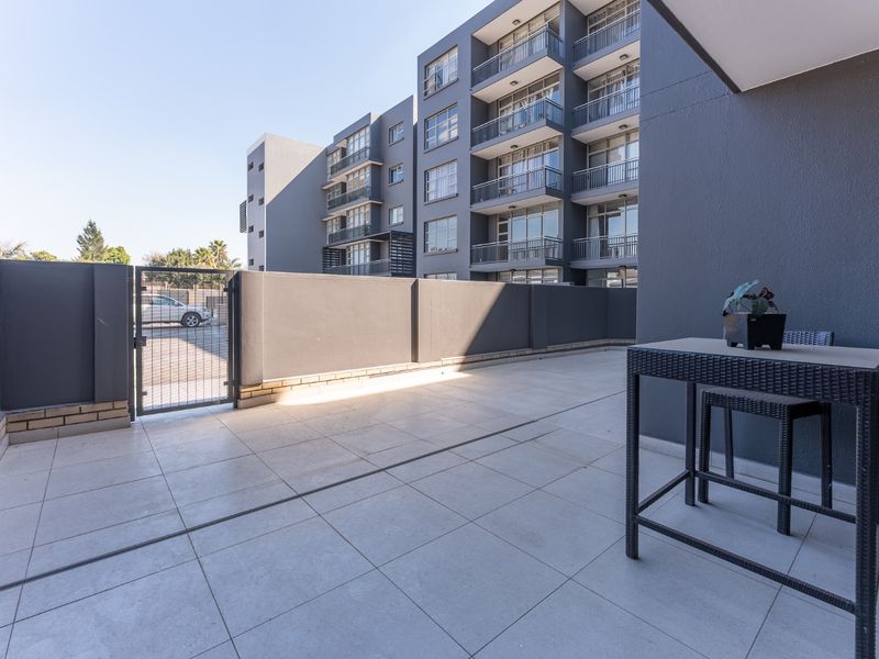A spacious, modern tiled balcony area with a boundary wall and metal gate, offering a clean outdoor space for relaxation.
