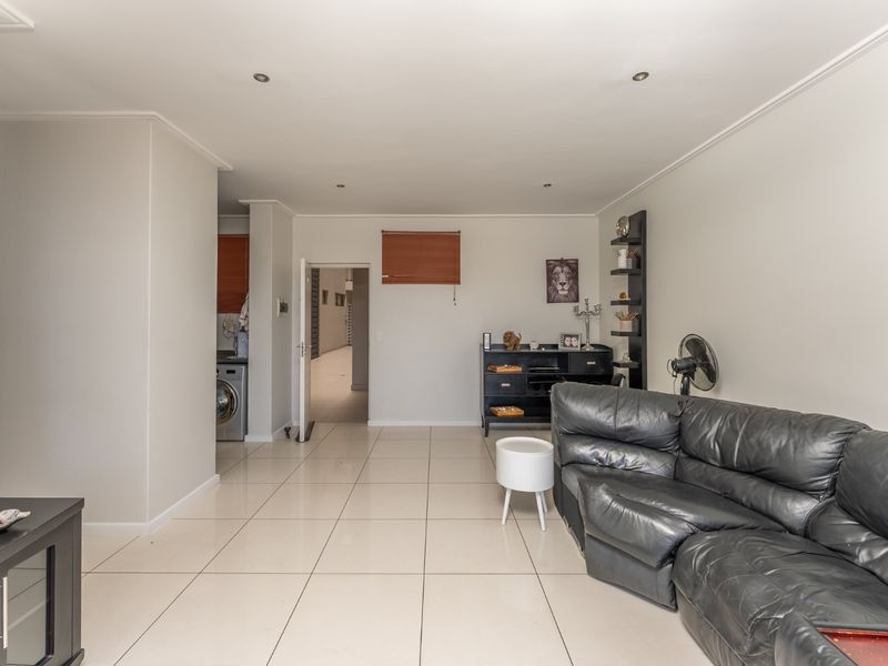 Open-plan living area featuring neutral tiled flooring, recessed downlighting, and a clean, functional layout connecting to adjacent utility and kitchen spaces.