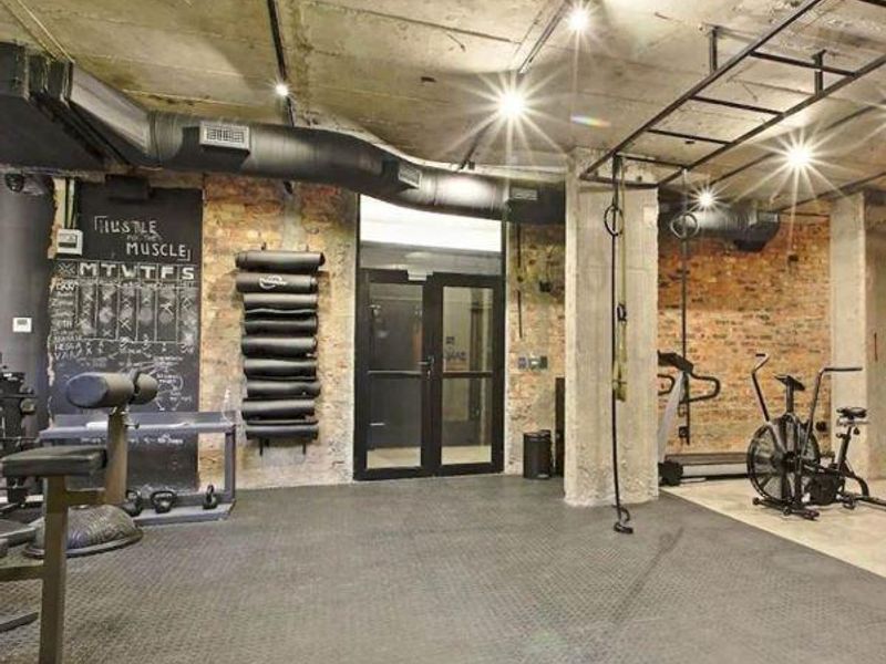 Industrial-style gym featuring exposed brick walls, concrete ceilings with ductwork, durable rubber flooring, and integrated lighting, creating a modern fitness environment.