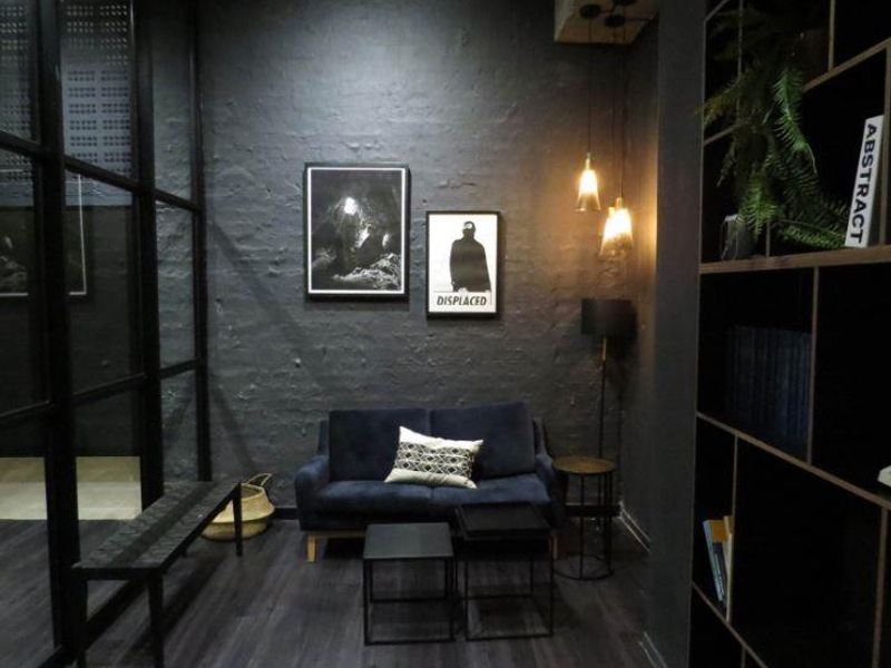 A modern, moody living area featuring dark textured walls, integrated shelving, and contemporary pendant lighting, creating a sophisticated and intimate atmosphere.