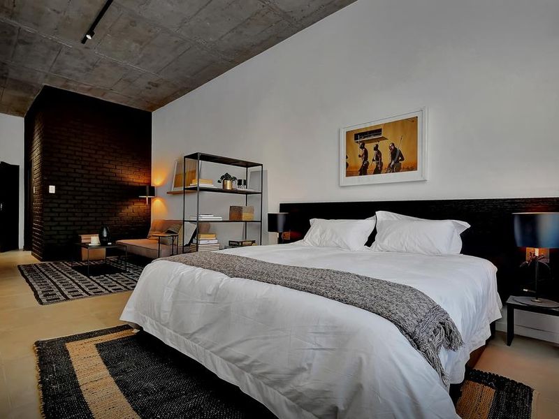 Spacious bedroom featuring an exposed concrete ceiling, a striking black brick feature wall, and modern tiled flooring with integrated track lighting.
