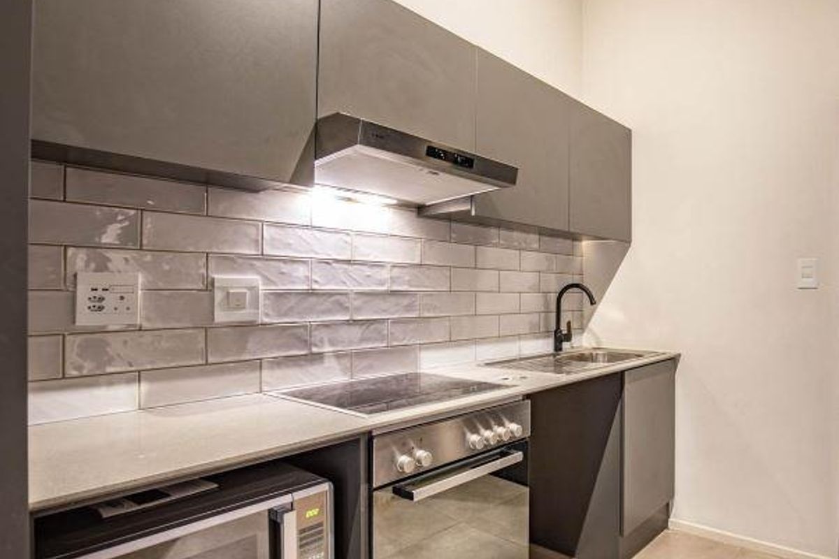 Modern kitchen featuring sleek grey cabinetry, subway tile backsplash, integrated stainless steel appliances, and stone countertops.