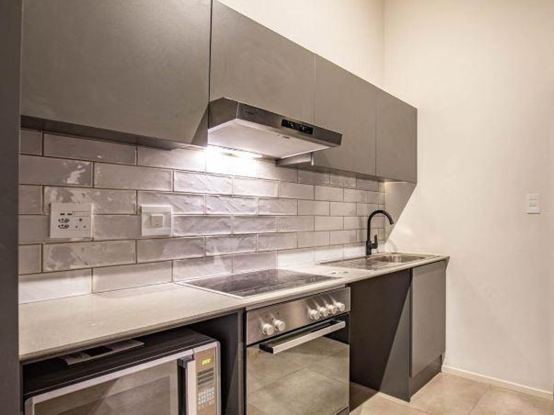 Modern kitchen featuring sleek grey cabinetry, subway tile backsplash, integrated stainless steel appliances, and stone countertops.