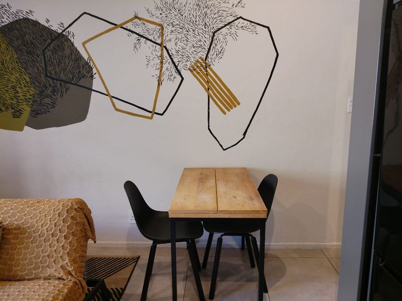 A living area featuring neutral tiled flooring and a decorative wall mural, providing a functional space for dining or relaxation.