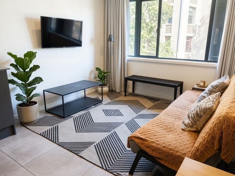 A bright and modern living room featuring large windows, neutral tiled flooring, and a wall-mounted television setup.