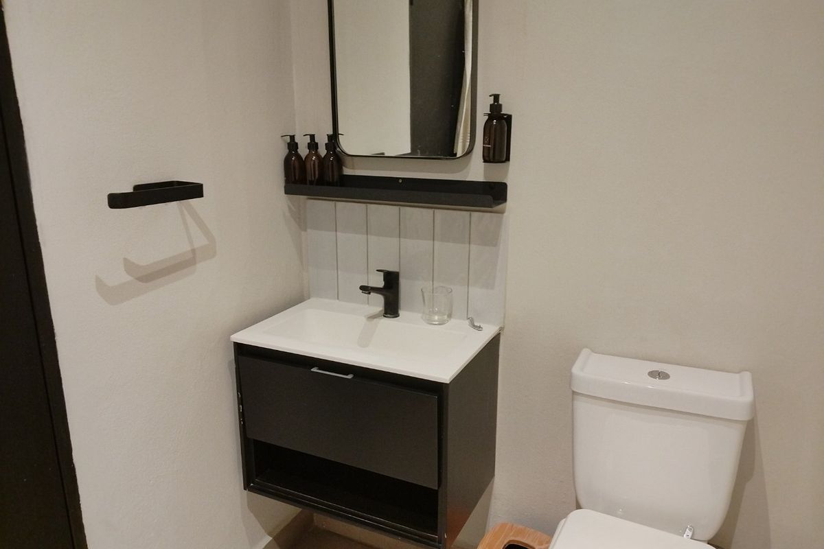 A modern bathroom featuring a wall-mounted vanity with basin, black faucet, tiled splashback, and a standard toilet.