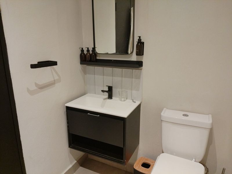 A modern bathroom featuring a wall-mounted vanity with basin, black faucet, tiled splashback, and a standard toilet.