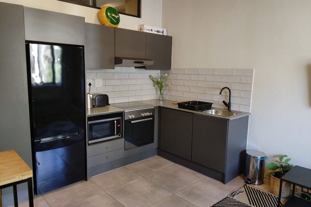 Modern compact kitchen featuring dark grey cabinetry, subway tile backsplash, integrated oven and hob, and a sleek stainless steel sink with matte black fixtures.