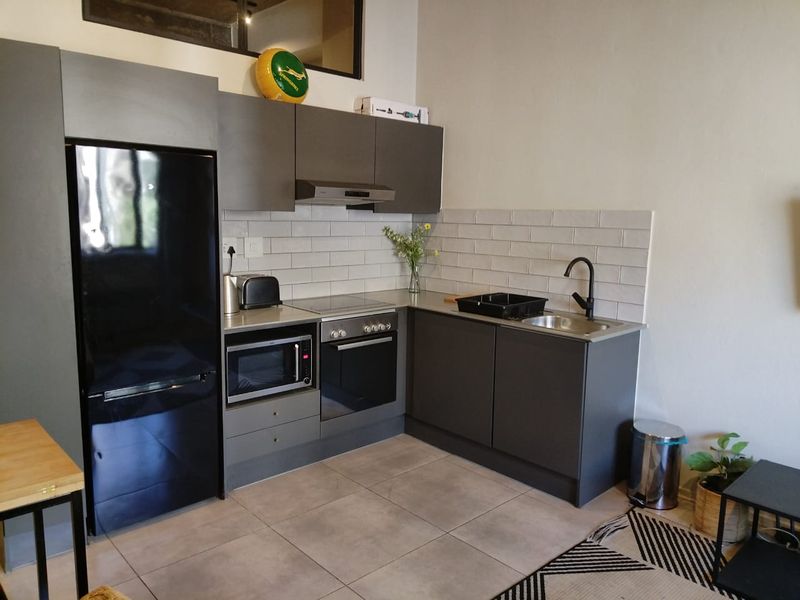 Modern compact kitchen featuring dark grey cabinetry, subway tile backsplash, integrated oven and hob, and a sleek stainless steel sink with matte black fixtures.