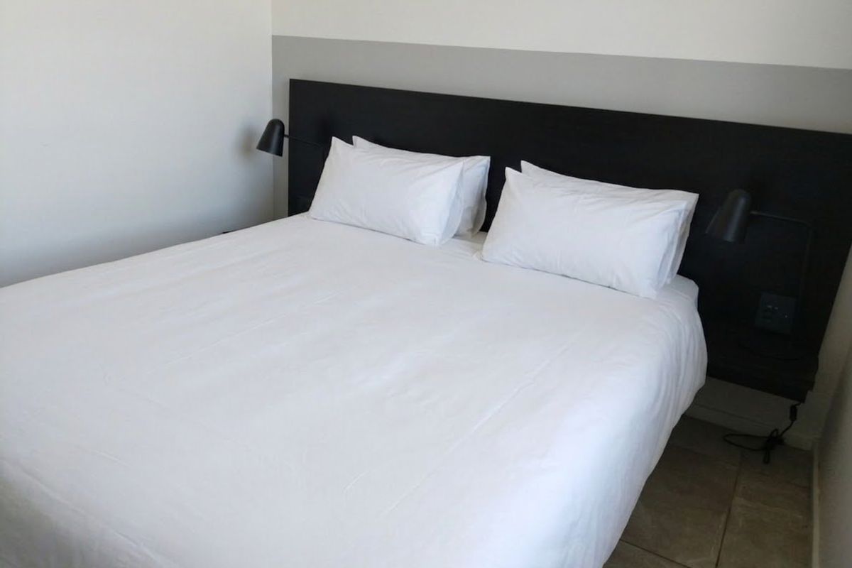 A clean bedroom featuring a built-in headboard with integrated wall-mounted reading lights and neutral tiled flooring.
