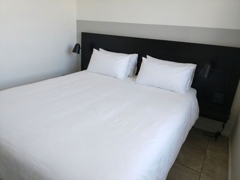 A clean bedroom featuring a built-in headboard with integrated wall-mounted reading lights and neutral tiled flooring.