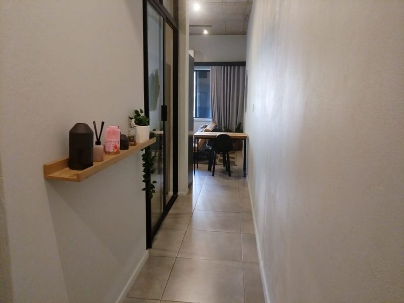 A well-lit hallway featuring tiled flooring and an exposed concrete ceiling, leading towards an open-plan living area with a sliding glass door entrance.