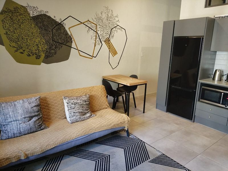 Modern open-plan living area featuring sleek grey cabinetry, integrated kitchen appliances, and neutral tiled flooring in a well-maintained apartment setting.