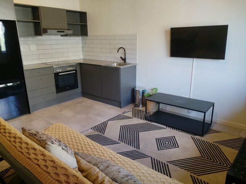 Modern open-plan living area featuring a compact kitchen with grey cabinetry, subway tile backsplash, and integrated appliances.