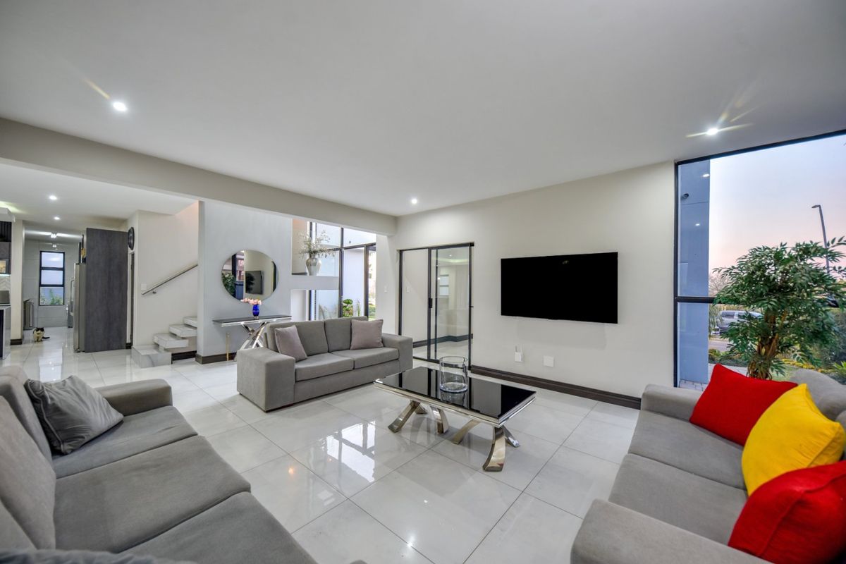 Spacious modern living room featuring polished porcelain tiles, recessed lighting, and large windows that provide ample natural light and a seamless flow to the exterior.