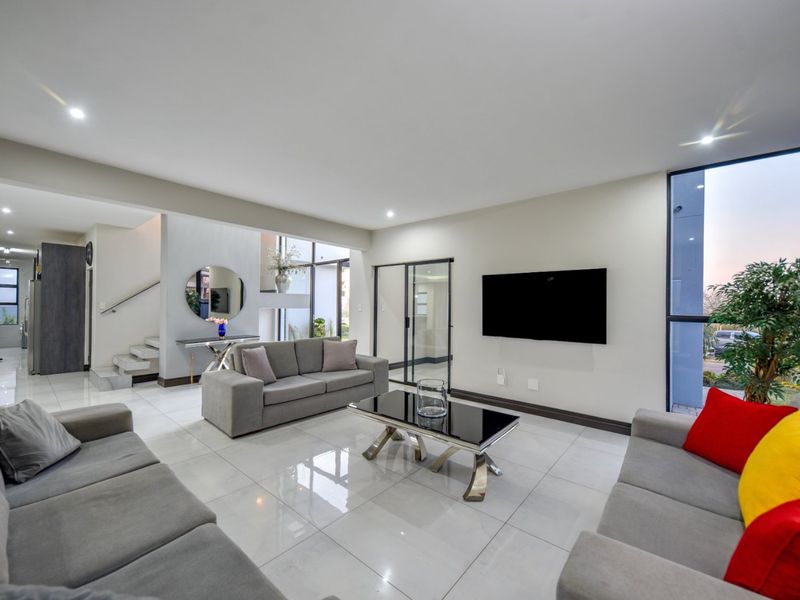 Spacious modern living room featuring polished porcelain tiles, recessed lighting, and large windows that provide ample natural light and a seamless flow to the exterior.