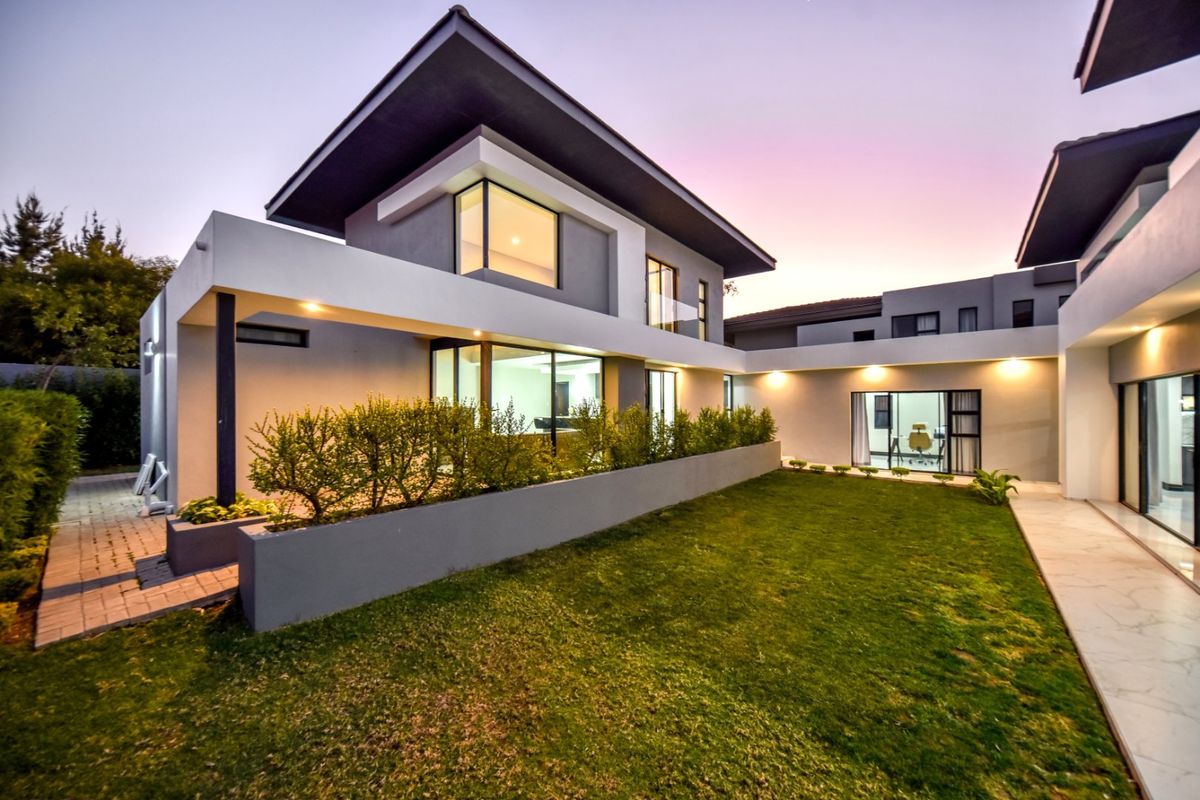 Modern rear exterior view of a contemporary two-story house featuring a landscaped garden, paved walkway, and large sliding glass doors.