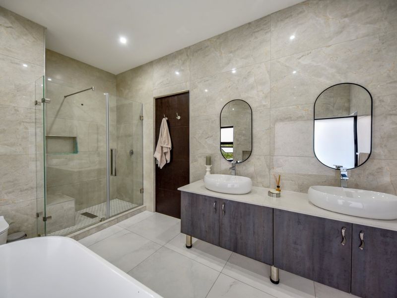 Modern bathroom featuring a double vanity with vessel sinks, a spacious walk-in shower with glass enclosure, and a freestanding bathtub with high-end tile finishes.