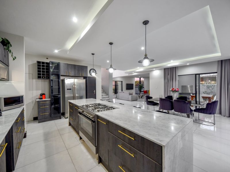Modern open-plan kitchen and dining area featuring a large stone-topped island, gas cooktop, sleek dark cabinetry, and polished tile flooring throughout.