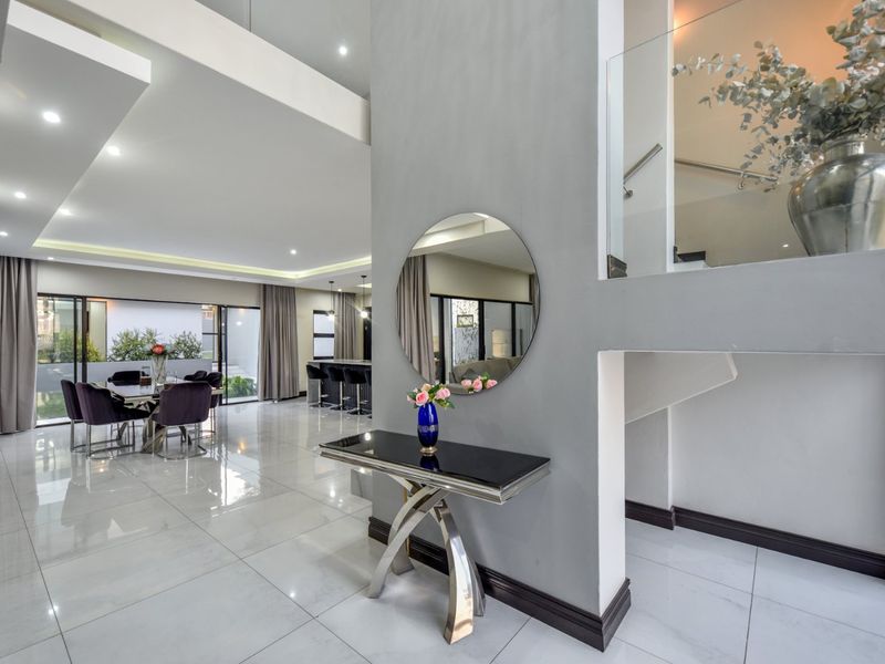 Spacious open-plan living and dining area featuring high-gloss porcelain tiles, modern recessed lighting, and a sleek glass staircase balustrade.