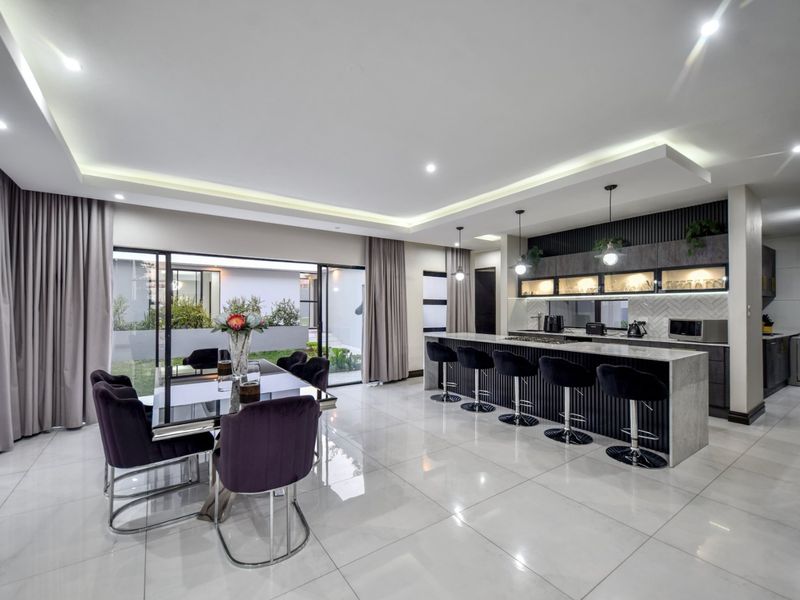 Modern open-plan living and kitchen area featuring a large stone island, sleek cabinetry, recessed lighting, and seamless access to the outdoor patio.