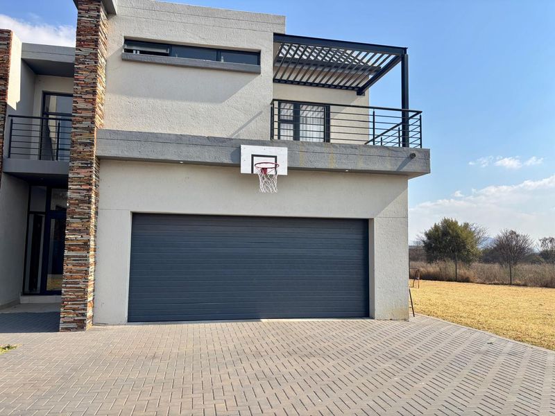 Modern double-story home exterior featuring a paved driveway, integrated garage, and an upper-level balcony with a metal pergola and stone feature wall.