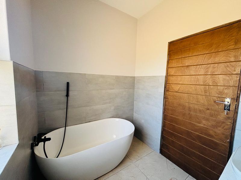 Modern bathroom featuring a sleek freestanding bathtub with matte black fixtures, complemented by neutral wall tiling and a natural timber door.