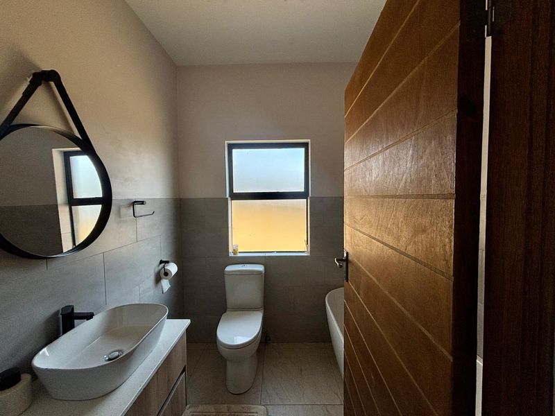 Modern bathroom featuring a vessel sink on a vanity cabinet, a toilet, and a bathtub with neutral wall and floor tiling.