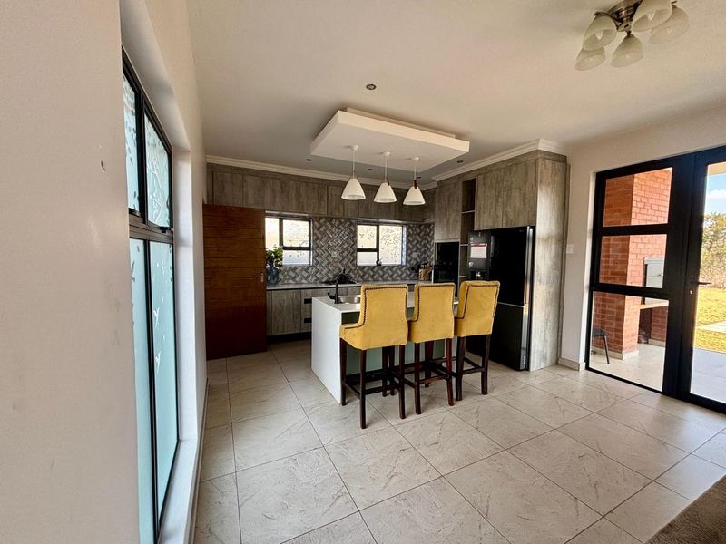 Modern kitchen featuring a central island, herringbone tile backsplash, custom cabinetry, and tiled flooring with direct access to an outdoor patio area.