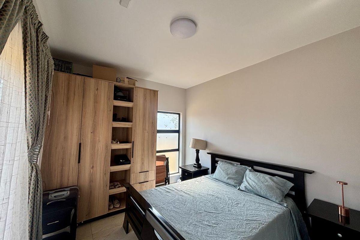 A well-maintained bedroom featuring neutral walls, tiled flooring, and a large built-in wooden wardrobe providing ample storage space.
