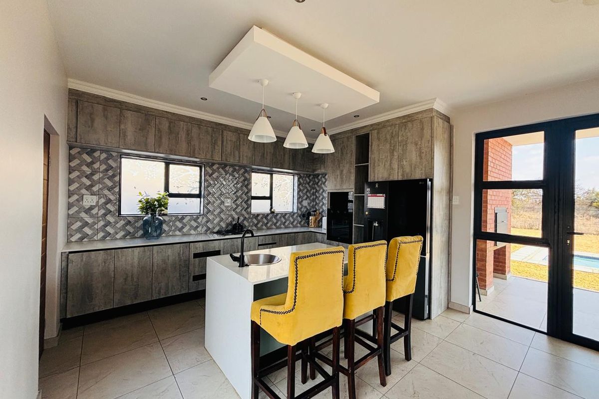 Modern kitchen featuring grey wood-look cabinetry, stone countertops, a central island with sink, and a stylish herringbone tiled backsplash.