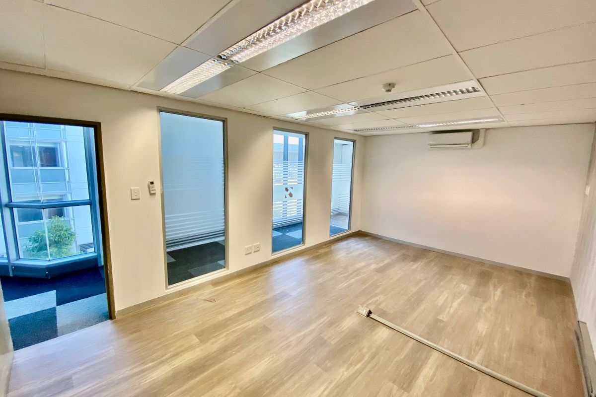 A bright, vacant commercial office space featuring vinyl flooring, recessed ceiling lighting, split-system air conditioning, and large windows providing natural light.