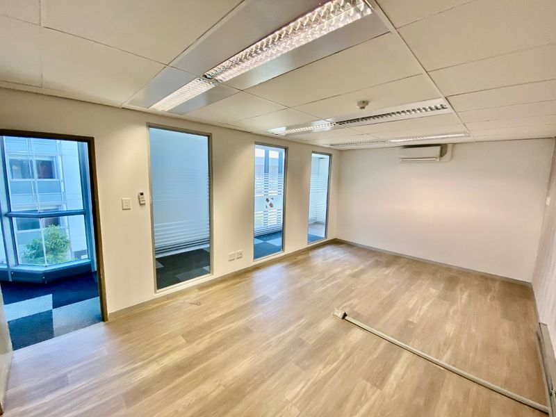 A bright, vacant commercial office space featuring vinyl flooring, recessed ceiling lighting, split-system air conditioning, and large windows providing natural light.