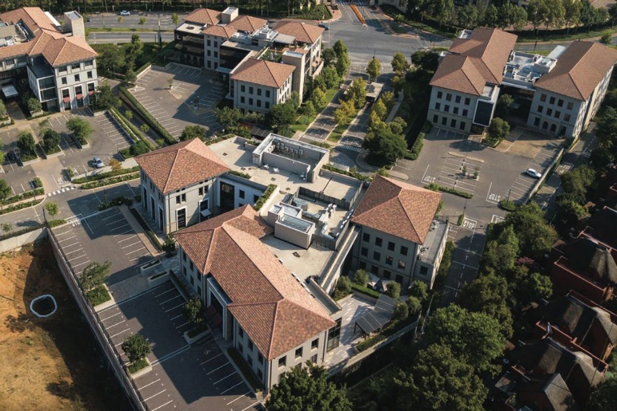 Aerial view of a commercial office park complex featuring multiple buildings with terracotta tile roofs, extensive parking facilities, and landscaped surroundings.