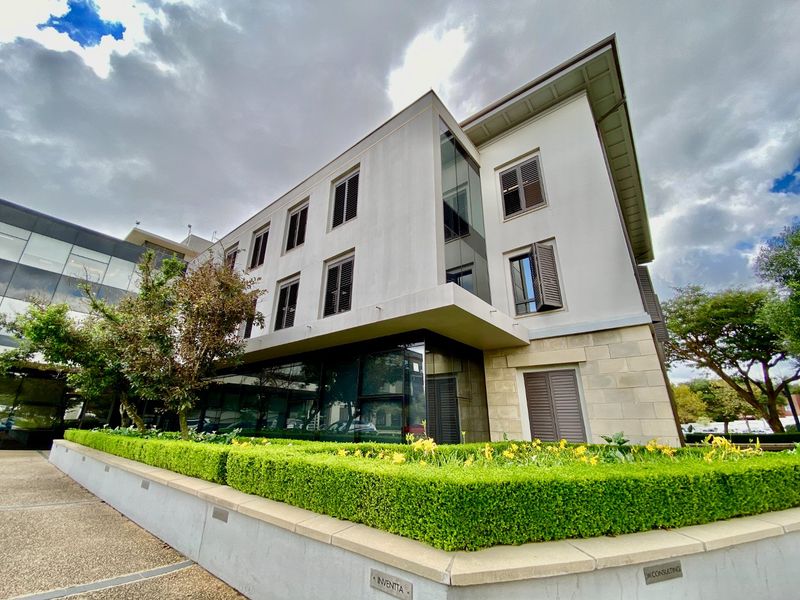 Modern commercial building facade featuring stone cladding, glass curtain walls, and well-maintained landscaped hedging at the entrance.
