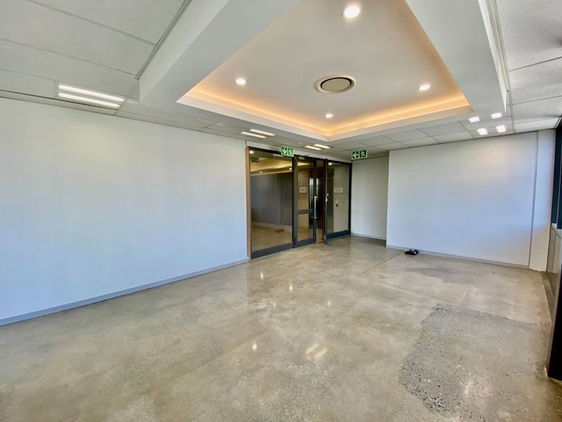 A spacious, empty commercial entrance lobby featuring polished concrete floors, recessed cove lighting, and glass double doors with emergency exit signage.
