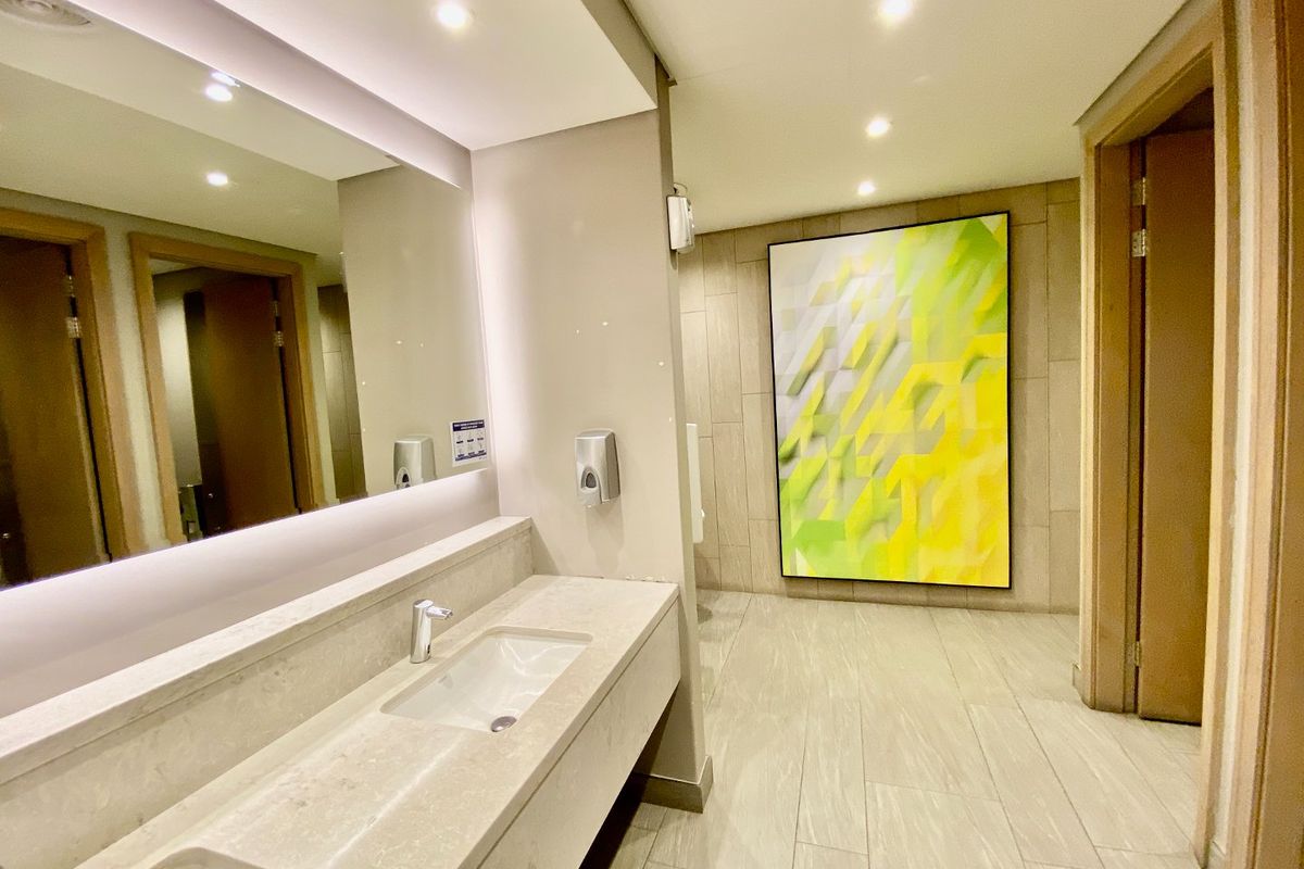Modern commercial bathroom featuring a double vanity with stone countertop, large wall mirror, recessed lighting, and neutral tiled finishes.