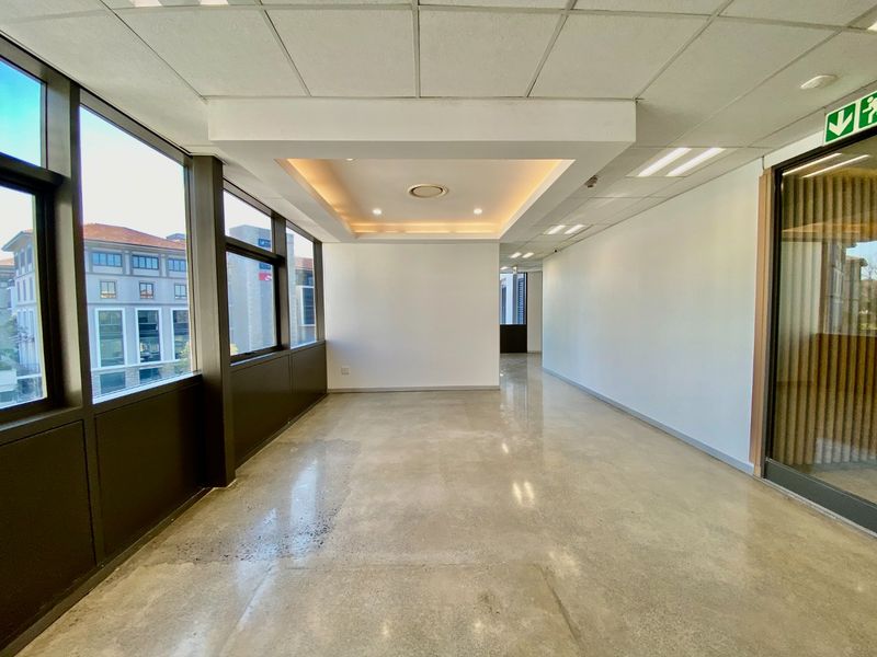 Modern, vacant commercial office space featuring polished concrete floors, a recessed tray ceiling with integrated lighting, and expansive windows providing natural light.