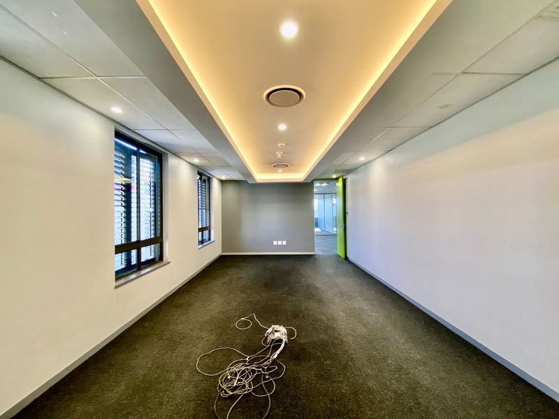 A bright, empty commercial office space featuring recessed cove lighting, suspended ceiling tiles, and large windows with aluminium frames.