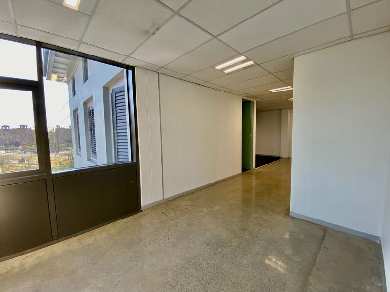 An empty, open-plan office space featuring polished concrete floors, suspended ceilings with recessed lighting, and large windows providing natural light.