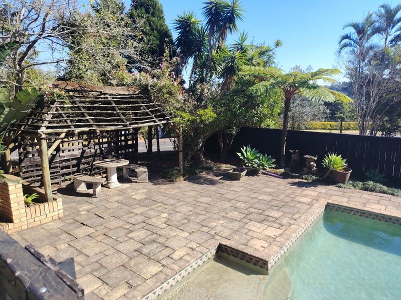 Outdoor pool area featuring a paved deck, swimming pool, and a weathered timber pergola set within a landscaped garden.