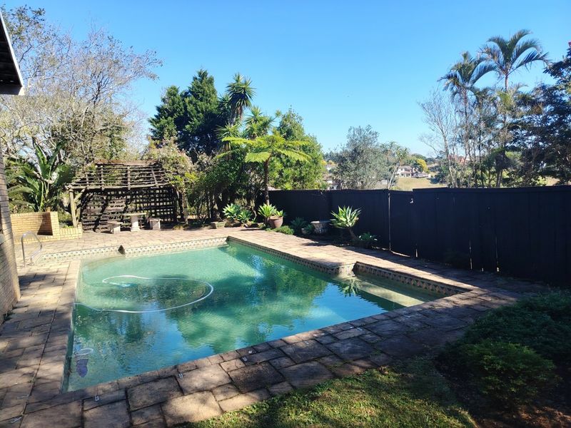 Outdoor pool area featuring a paved surround, timber privacy fencing, and a wooden pergola set within a landscaped garden.