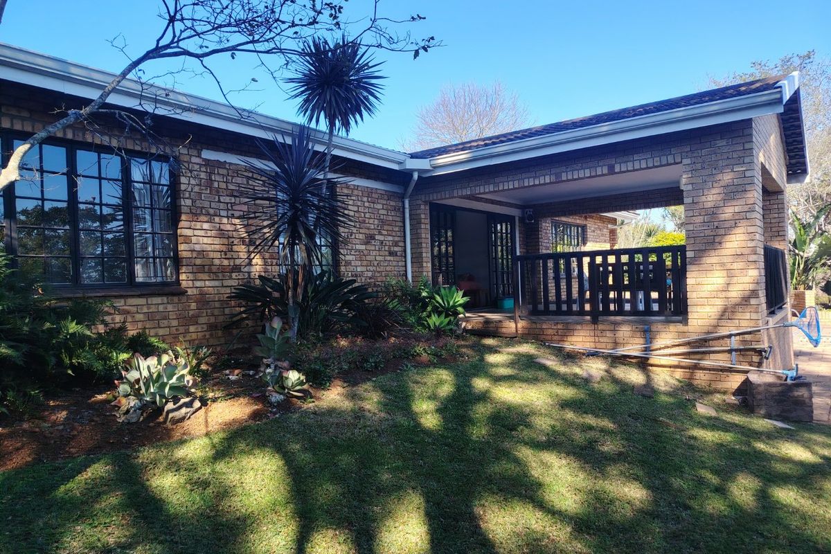Rear view of the property featuring a face brick facade, a covered patio area with timber balustrades, and established garden landscaping.
