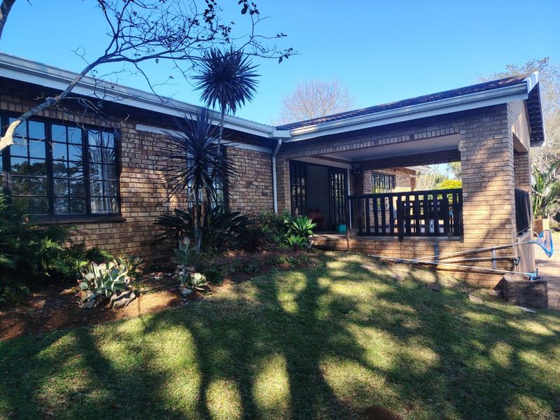 Rear view of the property featuring a face brick facade, a covered patio area with timber balustrades, and established garden landscaping.
