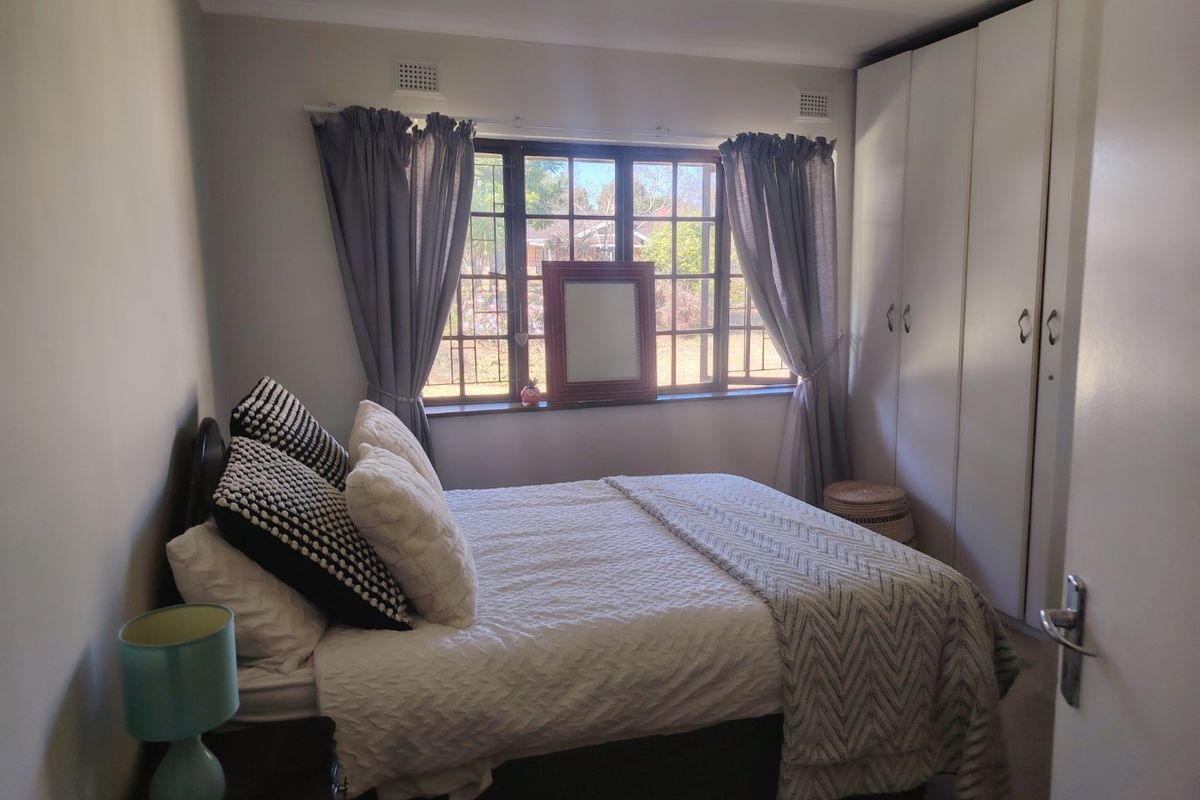 A functional bedroom featuring built-in cupboards and a steel-framed window, providing a comfortable and practical living space.
