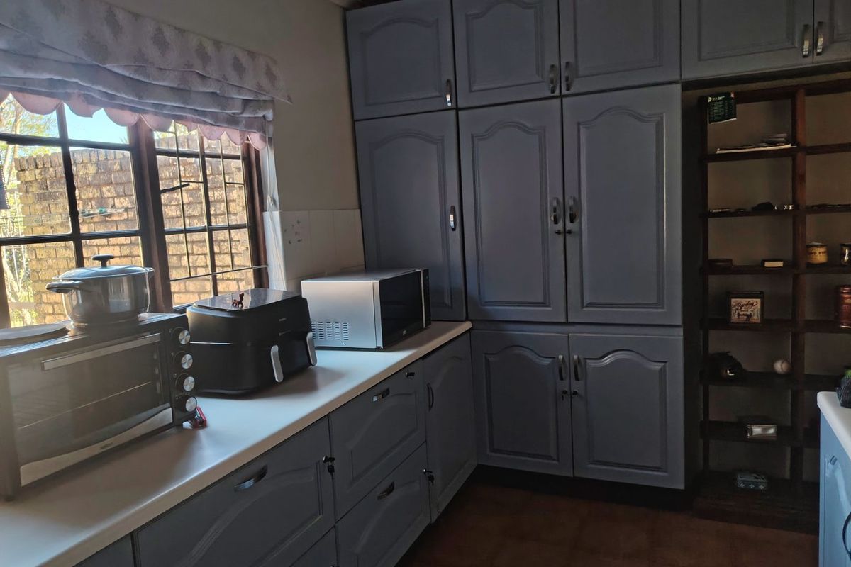A kitchen area featuring blue painted built-in cabinetry, laminate countertops, and a window with security bars.