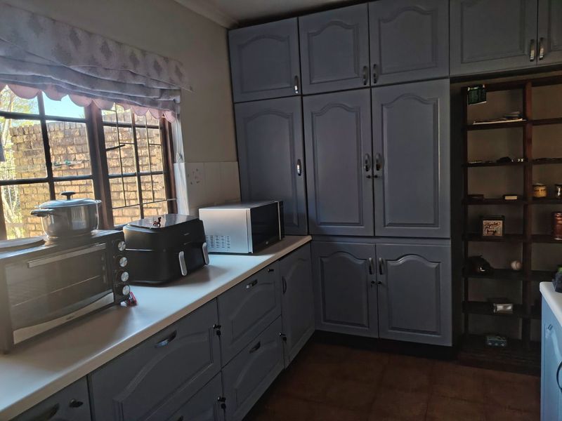 A kitchen area featuring blue painted built-in cabinetry, laminate countertops, and a window with security bars.